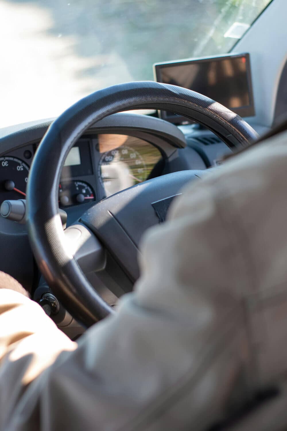 Person driving a vehicle, focusing on the steering wheel and dashboard, with sunlight visible through the windshield. - Home Instead