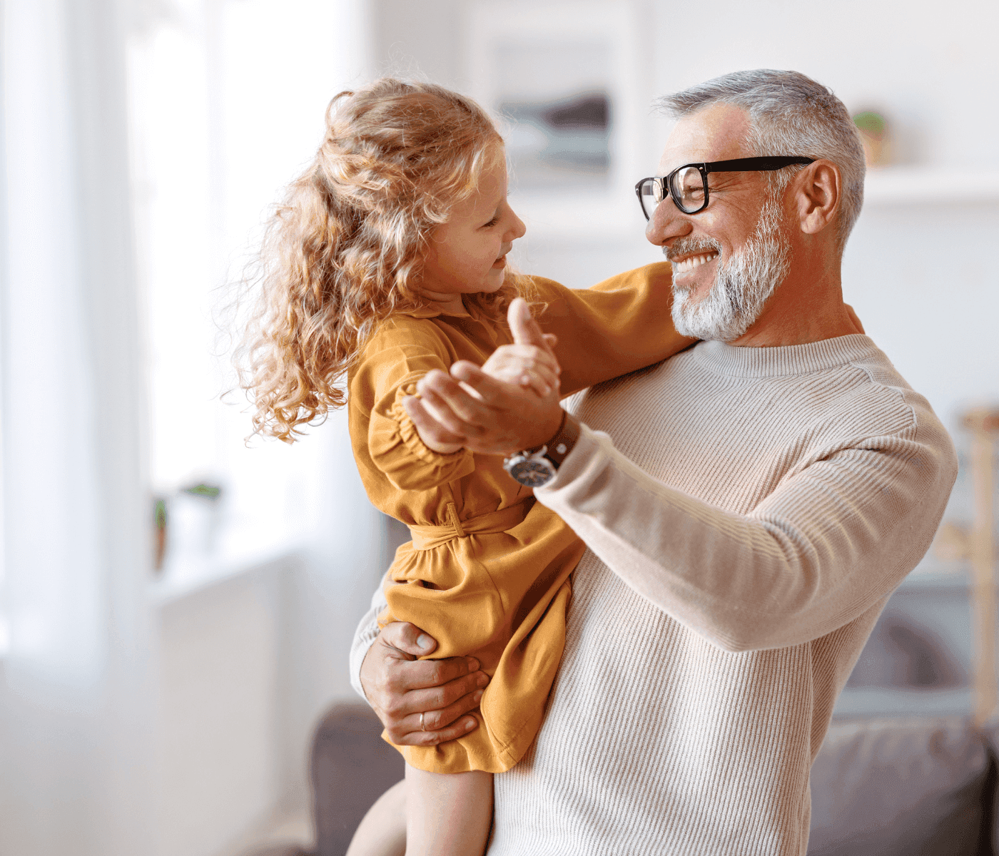 A smiling man holds an equally joyful young girl in his arms, enjoying a cheerful moment together in a bright room. - Home Instead