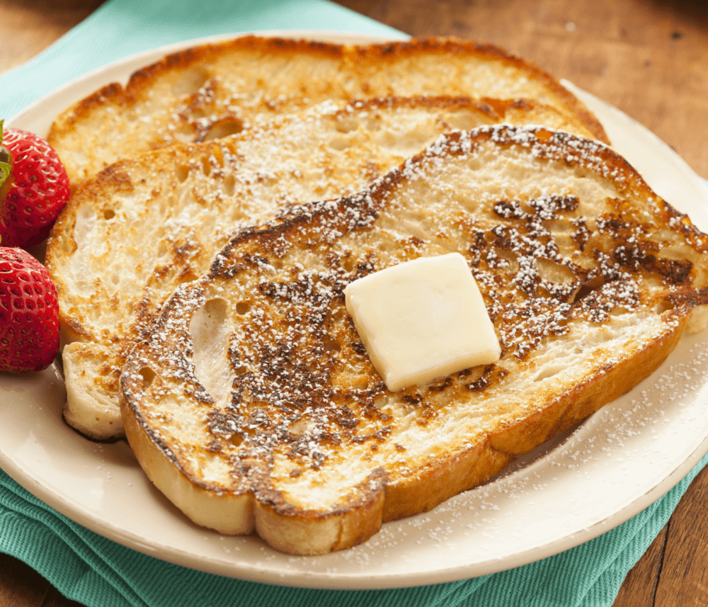 French toast with a pat of butter and powdered sugar on top, served with fresh strawberries on a plate. - Home Instead