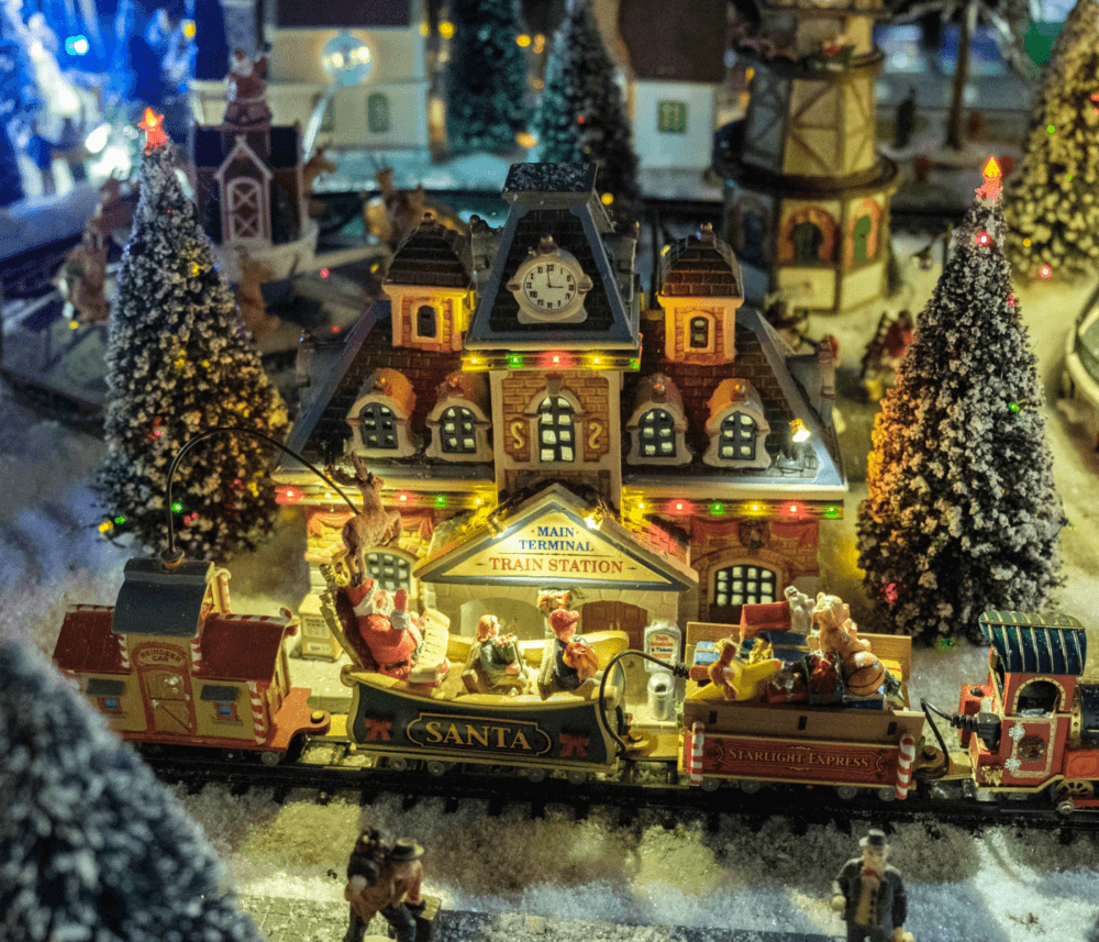 A miniature Christmas train station with Santa Claus and festive decorations in a snowy, illuminated scene. - Home Instead