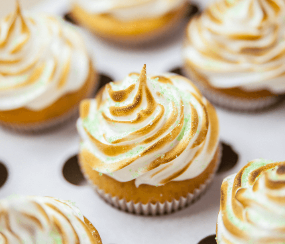 Close-up of cupcakes with swirled, toasted meringue frosting and green sugar sprinkles on a white background. - Home Instead