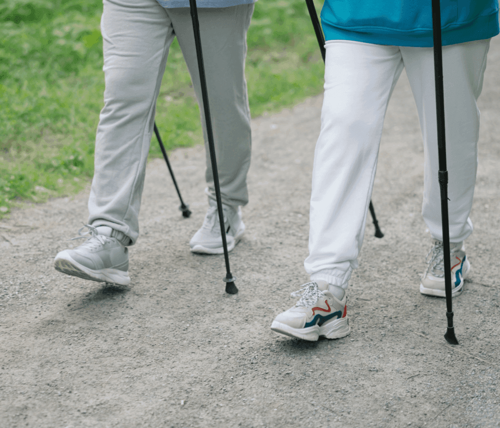 Two people walking on a trail with trekking poles, only their legs and footwear visible. - Home Instead