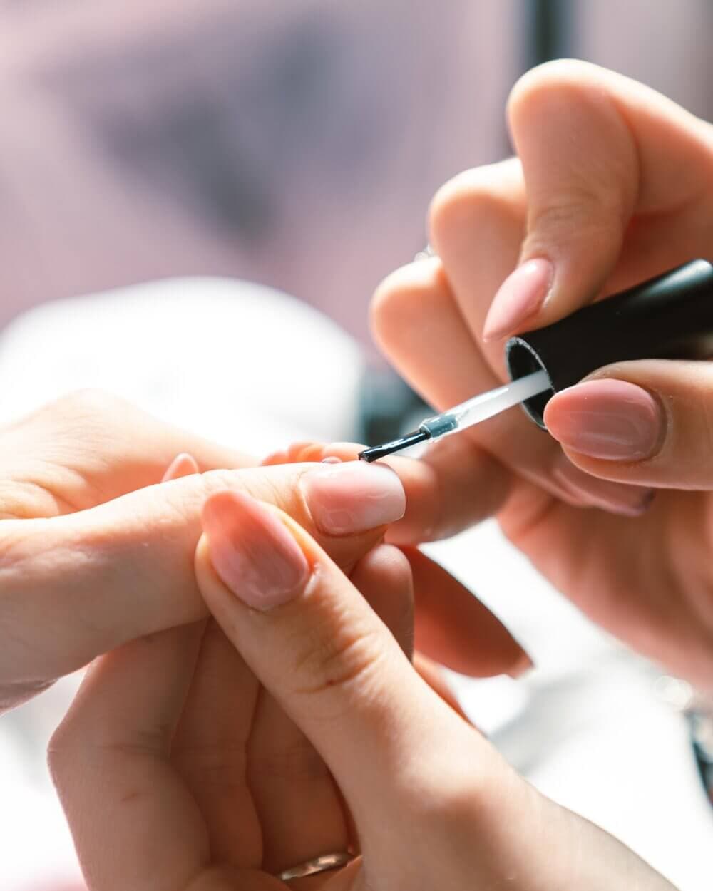 Close-up of a manicurist applying clear nail polish to a client's fingernail. - Home Instead