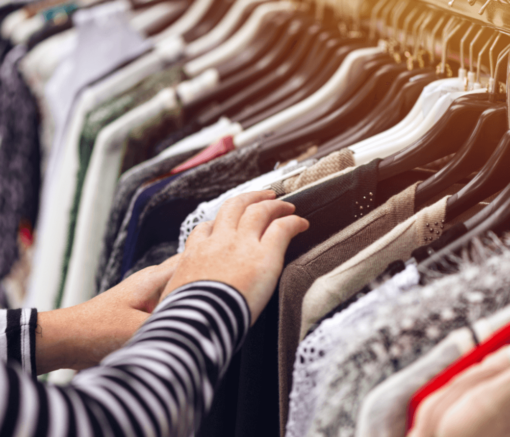 Person's hands browsing through clothes on hangers in a store. Various colors and styles are on the rack. - Home Instead
