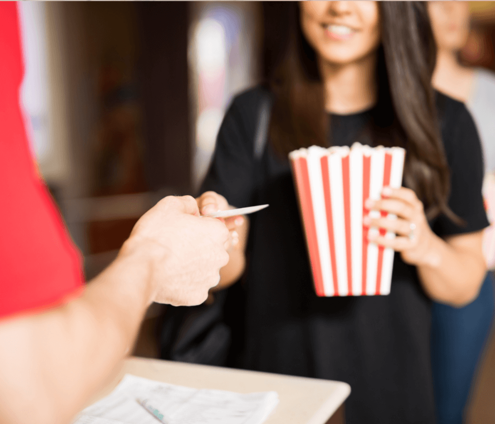 Person handing ticket to staff while holding a large tub of popcorn at a venue. - Home Instead