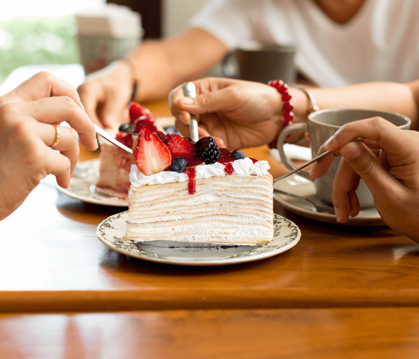 Three people enjoying slices of layered cake topped with berries at a wooden table, with coffee cups nearby. - Home Instead