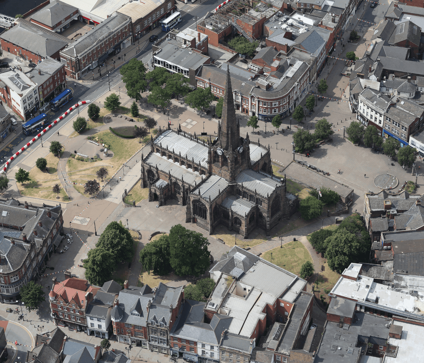 Aerial view of a historic church in the center of a town surrounded by buildings, roads, trees, and a small park. - Home Instead