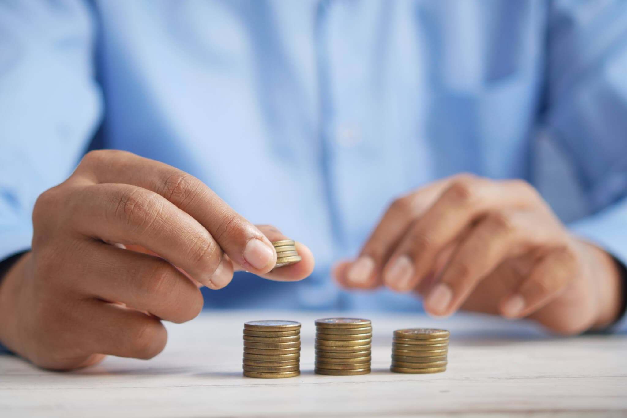 Person in blue shirt stacking and organizing piles of coins on a white surface. - Home Instead