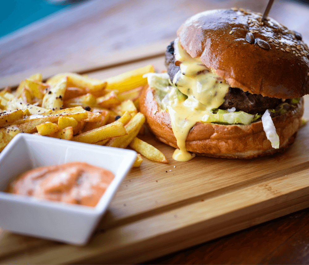 Burger with melted cheese, lettuce, and fries on a wooden board with a dipping sauce on the side. - Home Instead