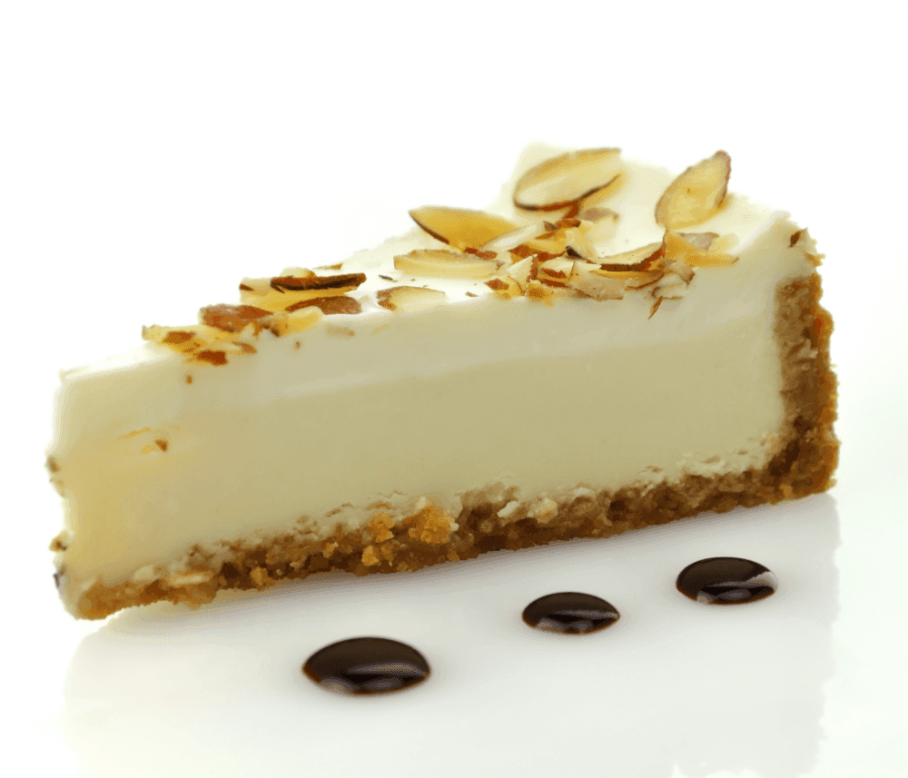 A slice of cheesecake topped with almond slices, served with three drops of chocolate sauce on a white plate. - Home Instead