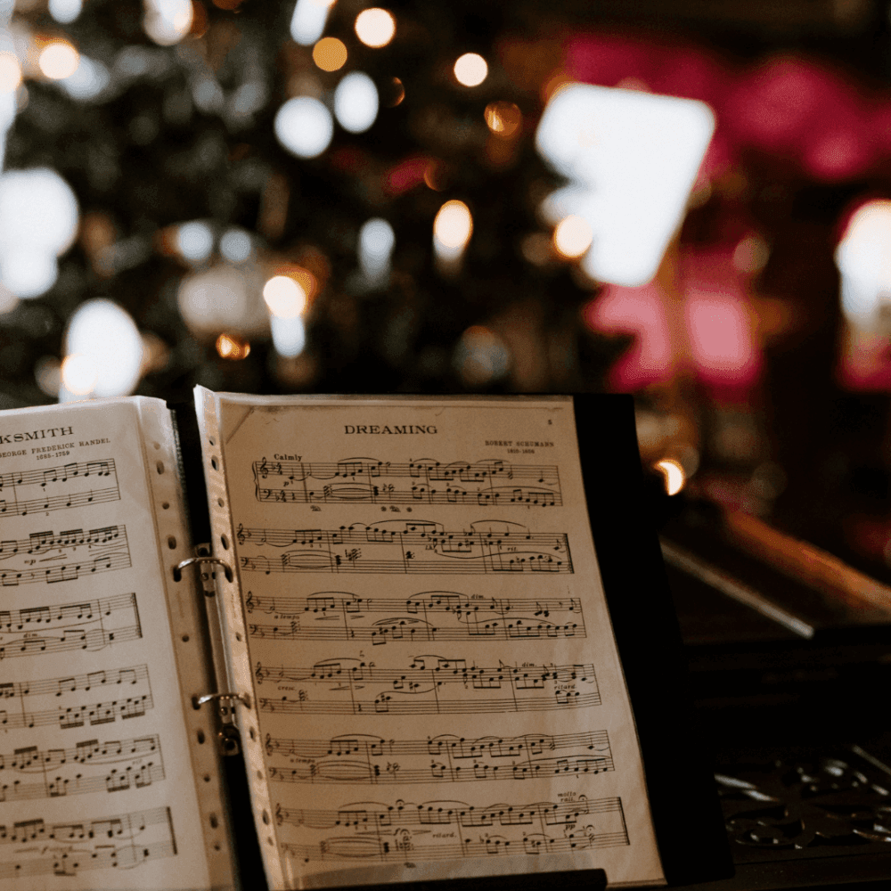 Open sheet music titled "Dreaming" on a music stand, with a blurred background of Christmas lights and decorations. - Home Instead