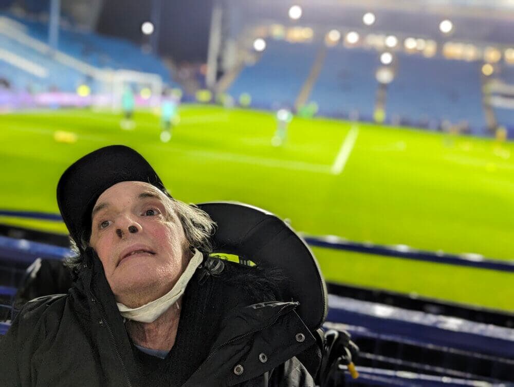 A person in a wheelchair is at a football stadium, with the field and stands visible in the background at night. - Home Instead
