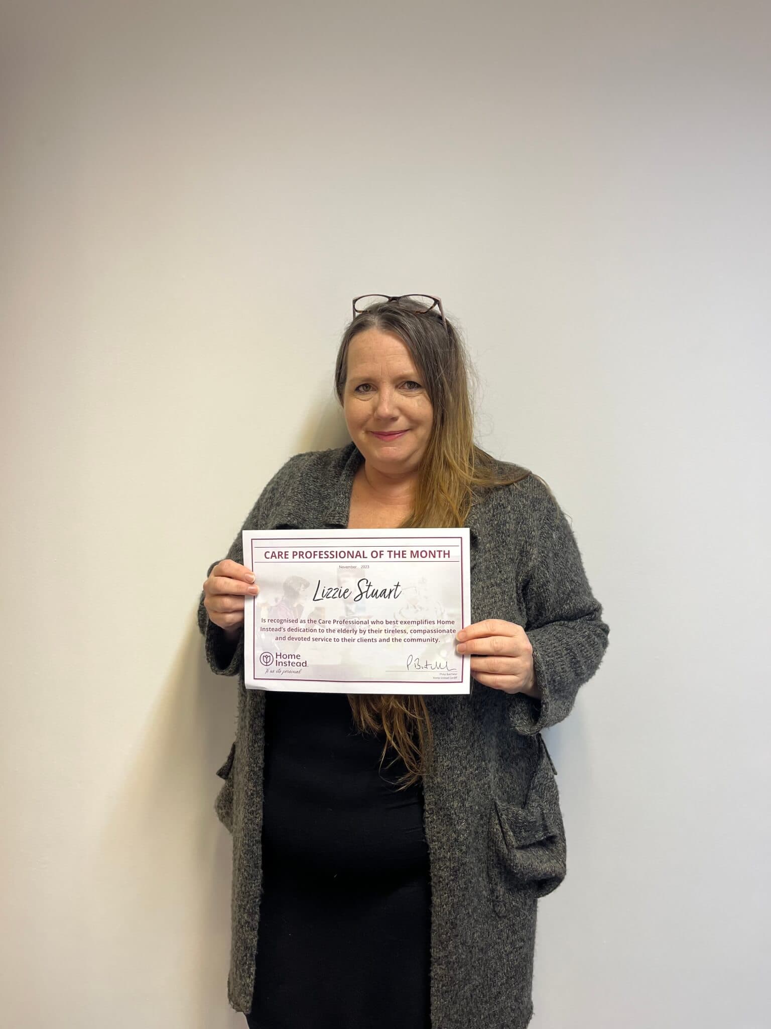 A person holding a certificate that reads "Care Professional of the Month" against a plain background. - Home Instead