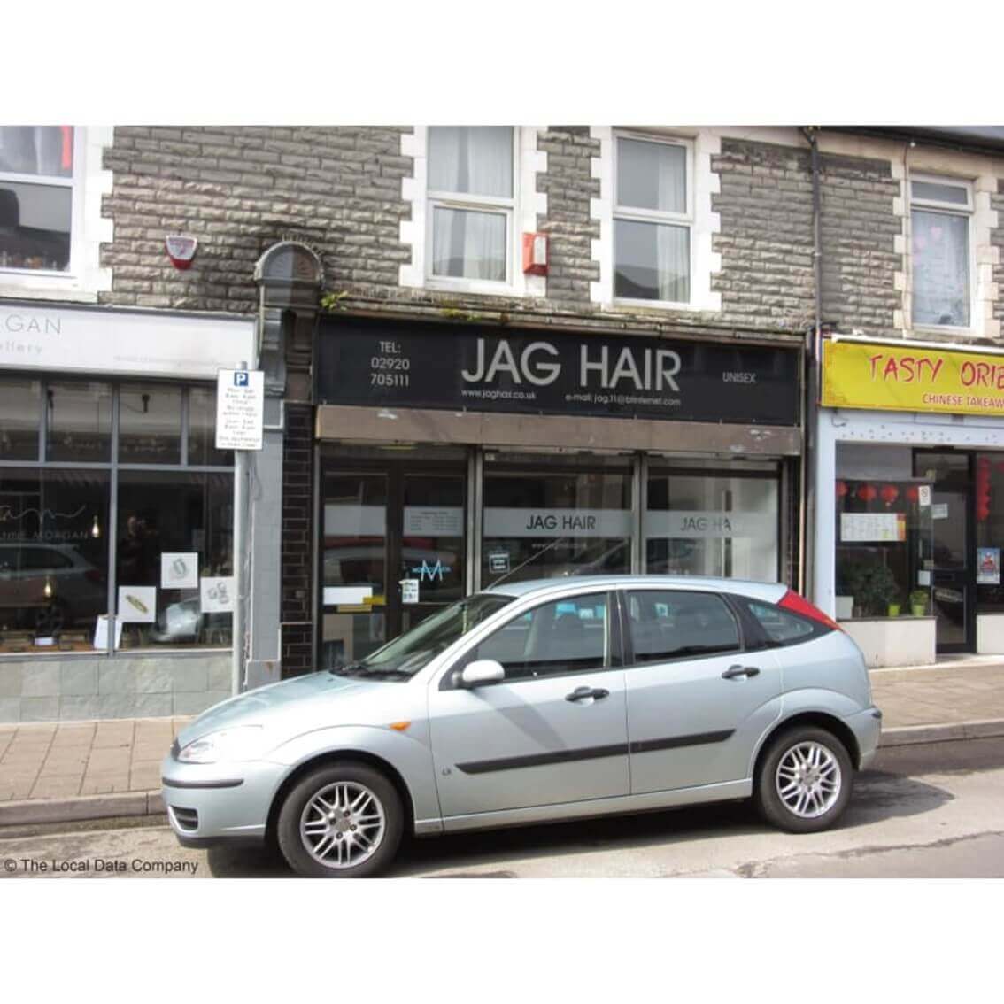 A silver car is parked in front of "JAG HAIR" salon on a street with other shops visible in the background. - Home Instead