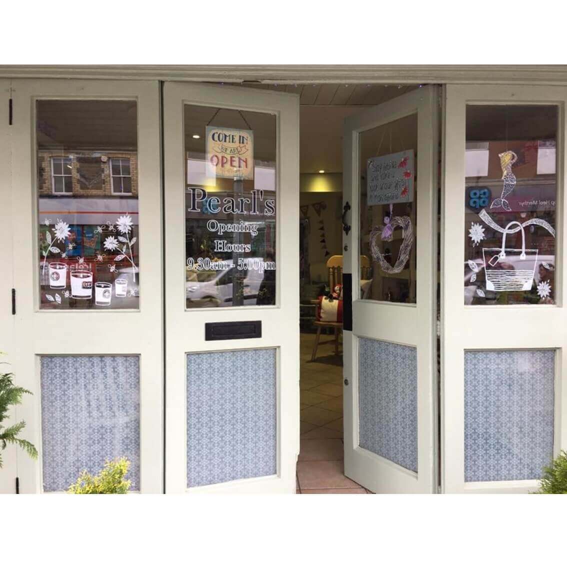 Front entrance of a quaint shop named "Pearl's" with glass doors decorated with festive designs and an open sign. - Home Instead