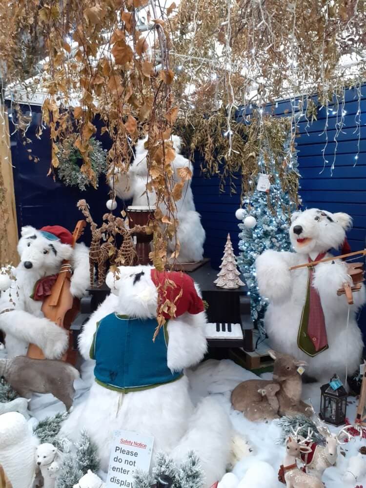 Four stuffed polar bears, dressed in festive attire, playing instruments in a snowy, holiday-themed display scene. - Home Instead
