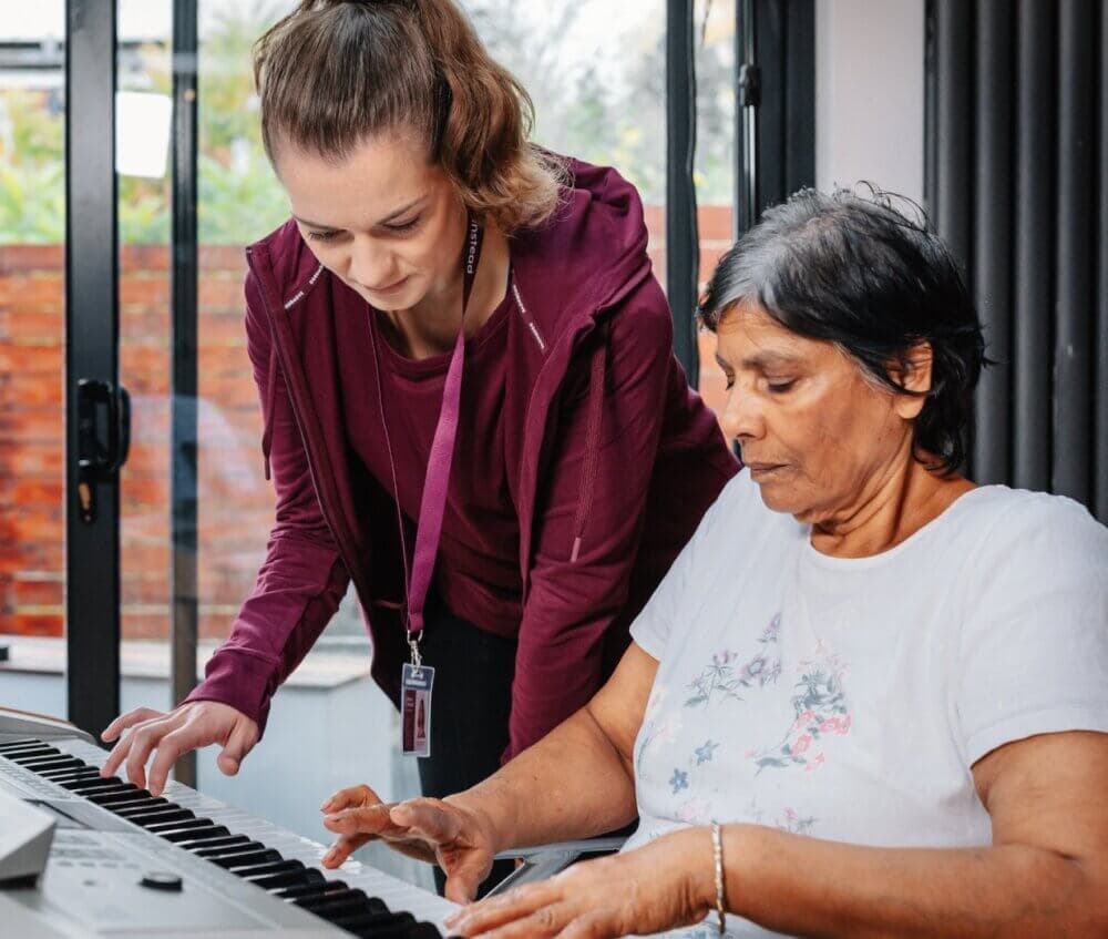 Two men, one older and one younger, washing dishes together in a cozy kitchen, smiling and conversing. - Home Instead