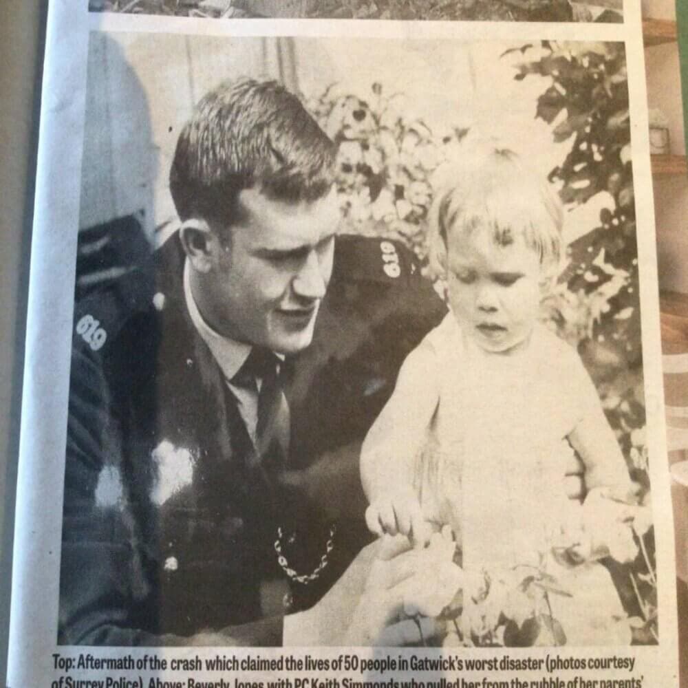 A policeman comforts a young child after a fatal crash at Gatwick, as seen in a black-and-white newspaper photo. - Home Instead