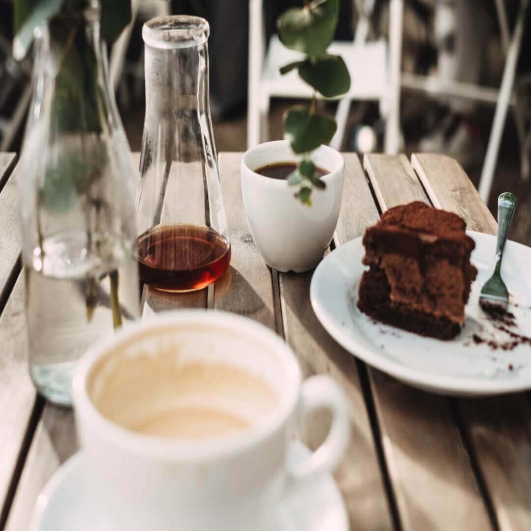 Coffee with milk in a mug, black coffee in a cup, a slice of chocolate cake, and a glass jug on a wooden table. - Home Instead