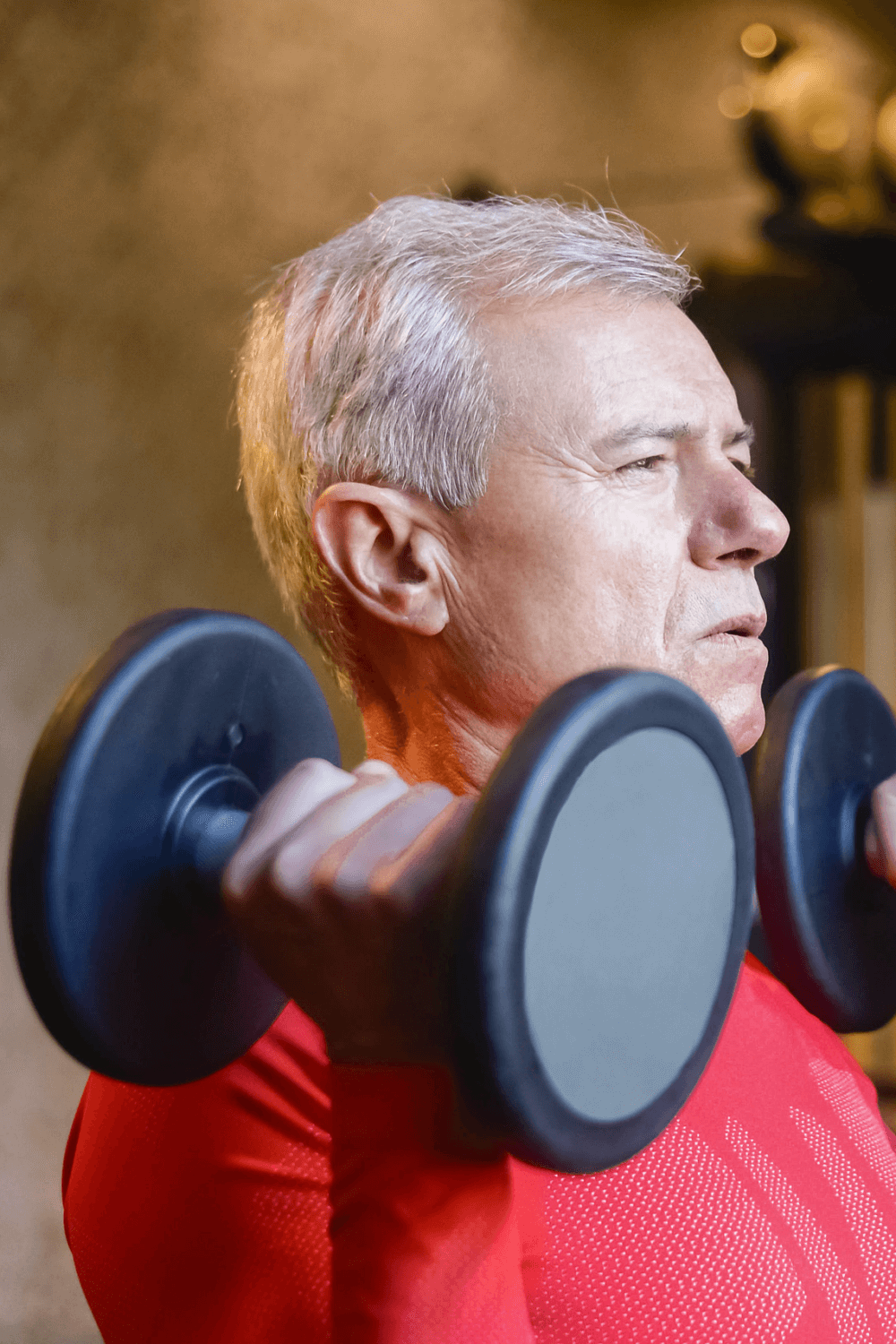 Elderly man in a red shirt lifting weights indoors, focused on the exercise. - Home Instead