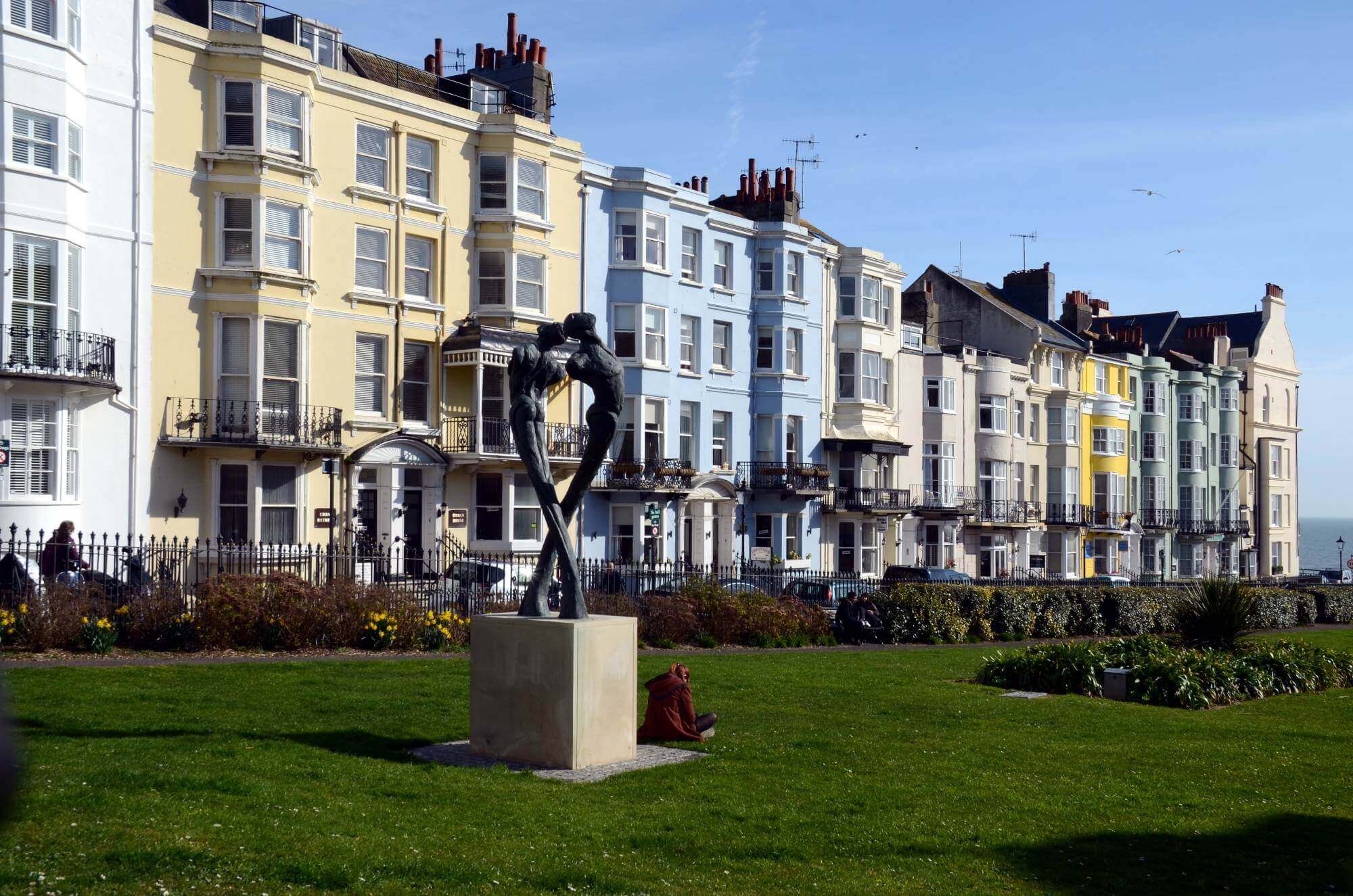 A line of colorful buildings along a grassy area with a modern sculpture in front, under a clear blue sky. - Home Instead
