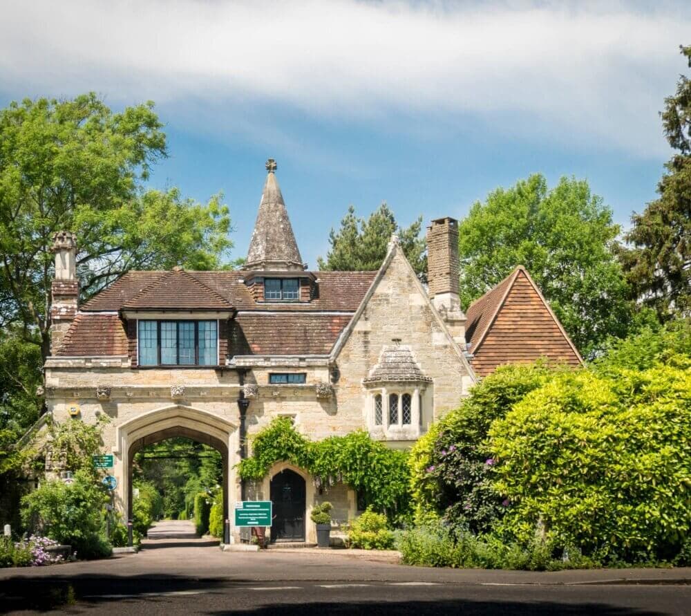 A stone building with an arched doorway, peaked roofs, and lush greenery on a sunny day. - Home Instead