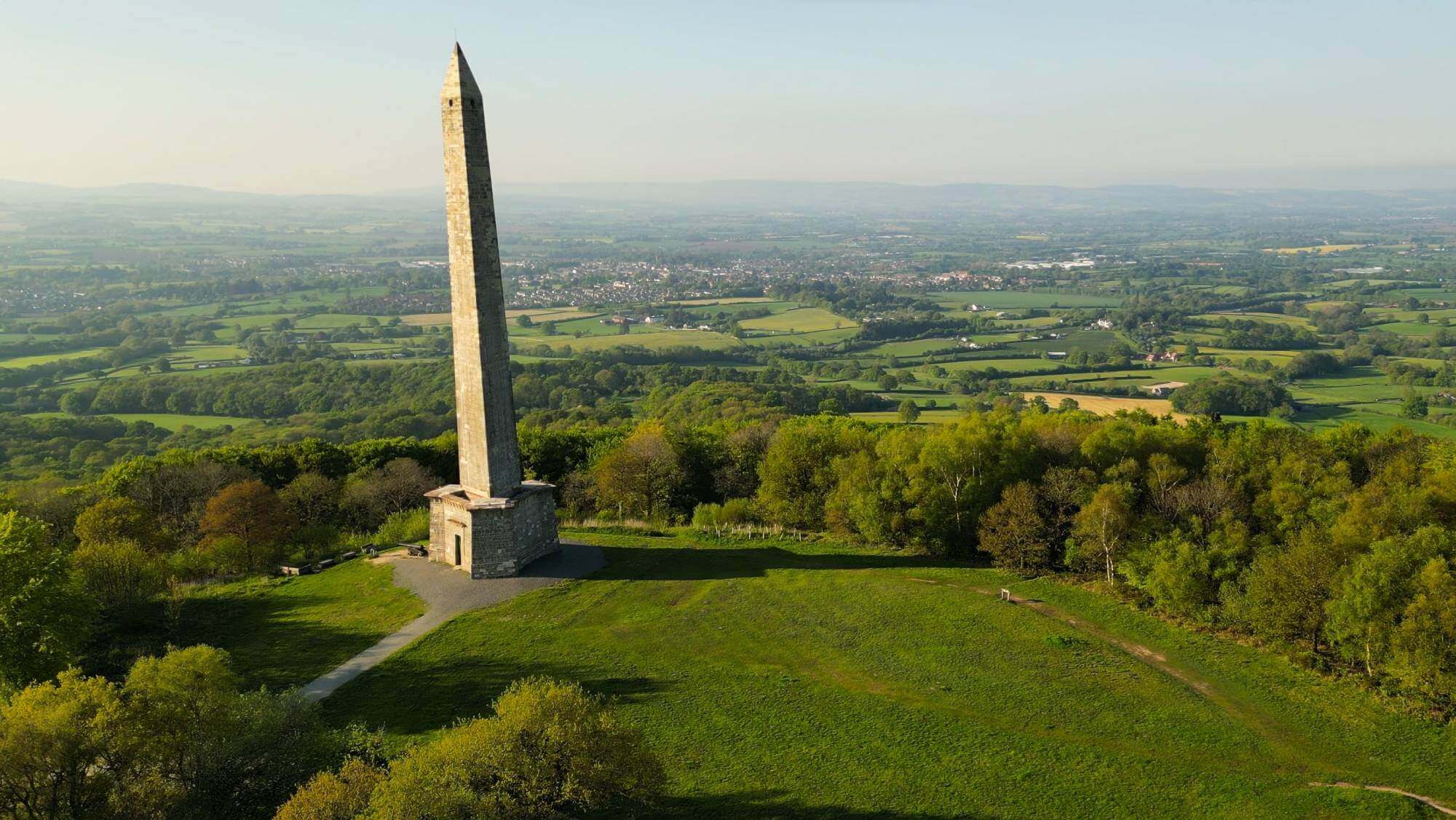 Aerial view of a tall obelisk surrounded by lush green fields and trees, under a clear blue sky. - Home Instead