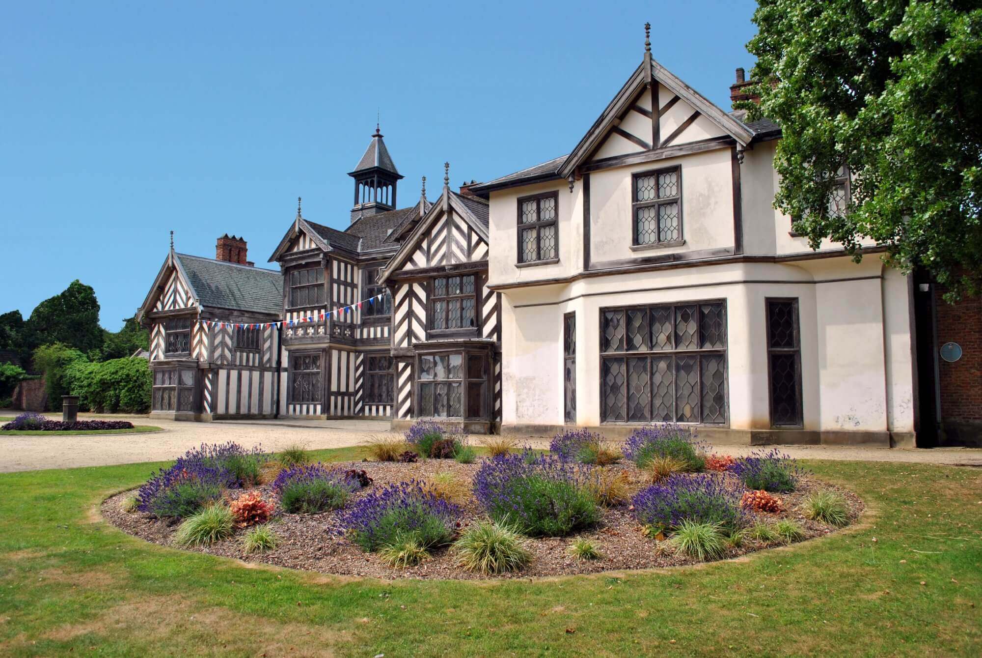 Historic half-timbered building with a decorative garden in the foreground, under a clear blue sky. - Home Instead