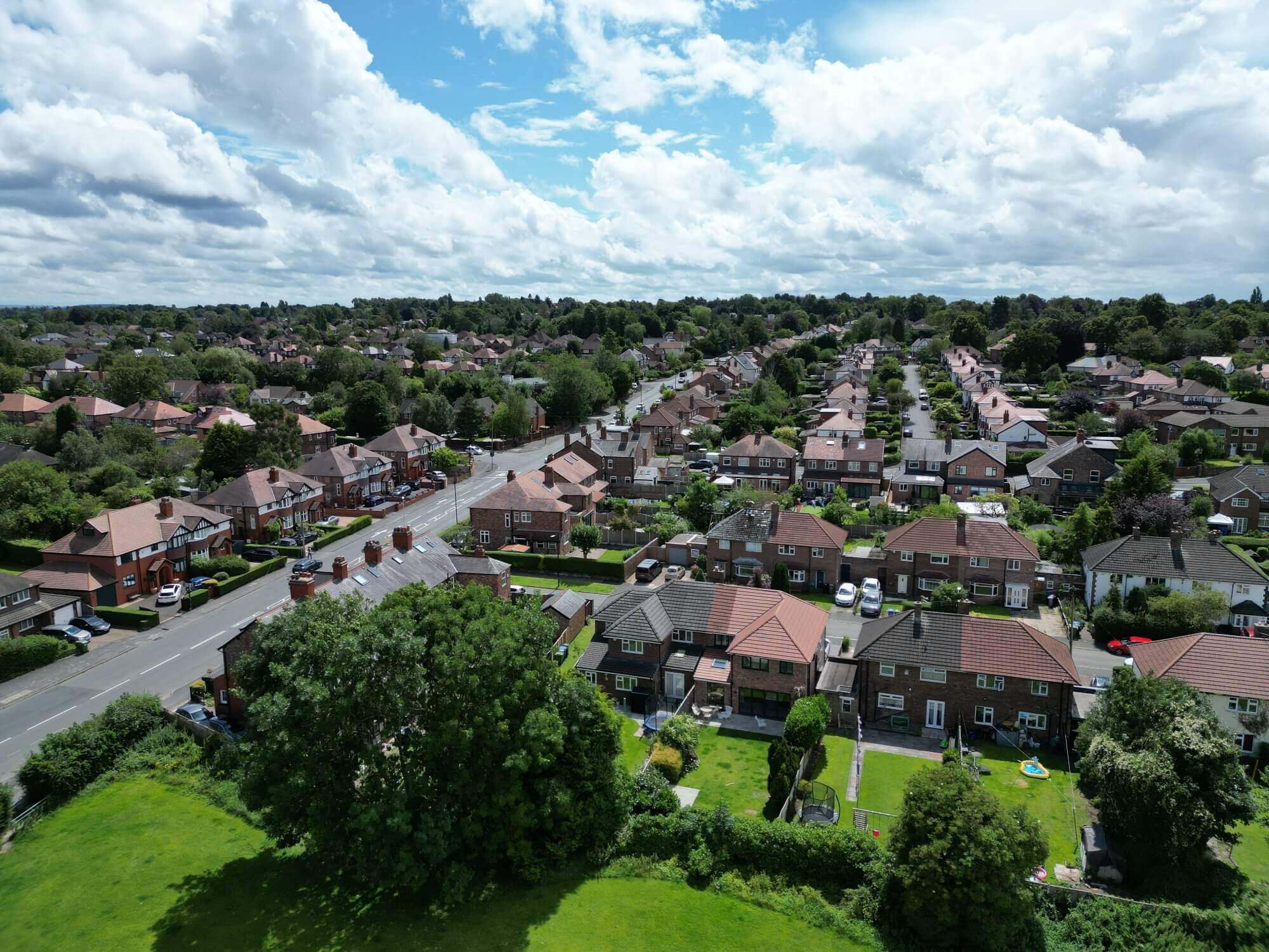 Aerial view of a suburban neighborhood with rows of houses, trees, and a partly cloudy sky. - Home Instead