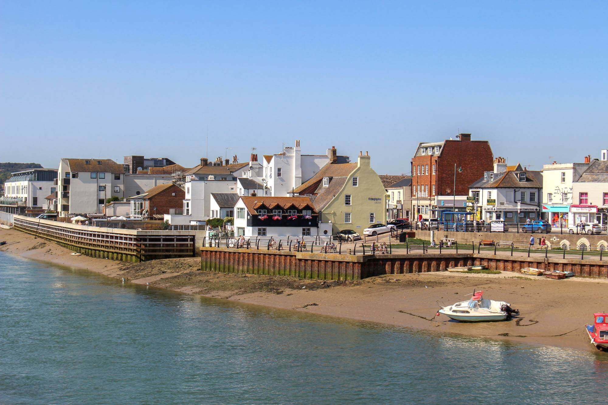 Coastal town with buildings along the shore, boats docked on the sandy beach, and a bright blue sky above. - Home Instead