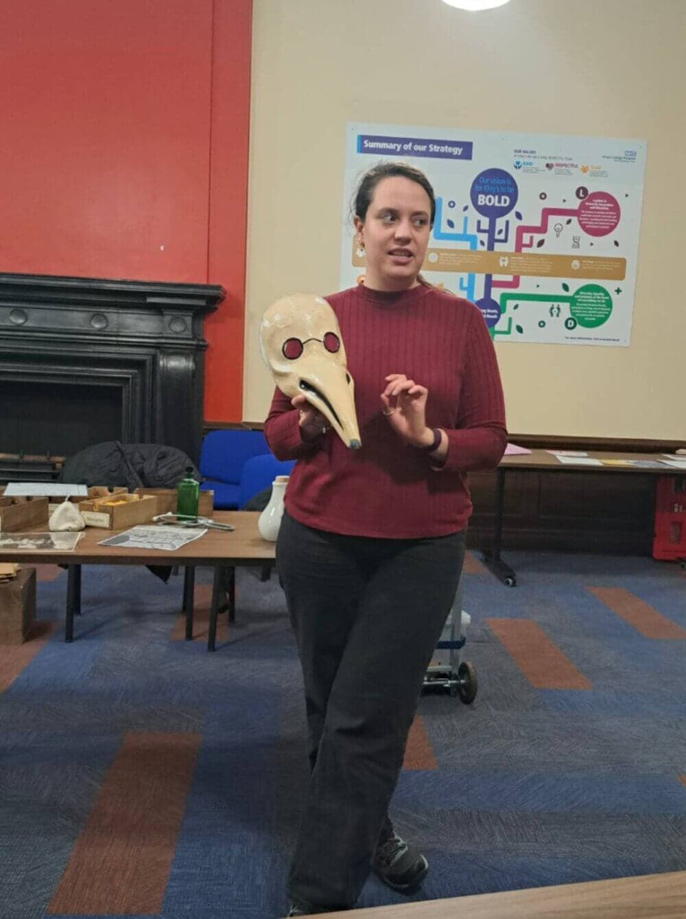 Person holding a plague doctor mask in a room with informational posters on the wall. - Home Instead