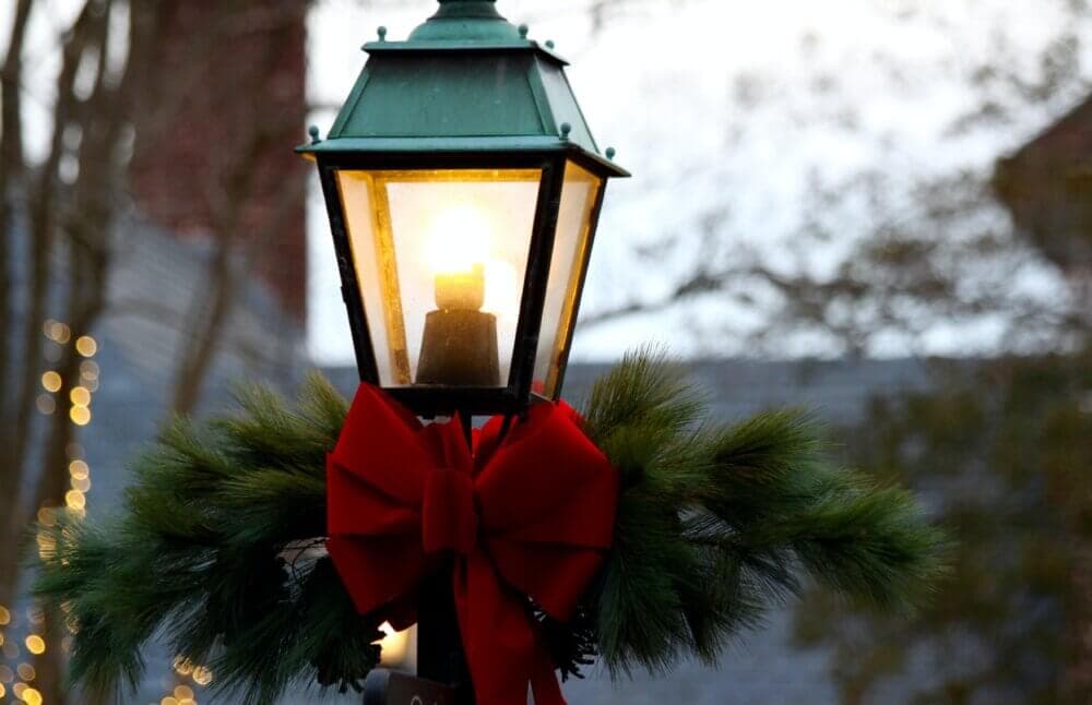 A lit lantern adorned with a red bow and greenery, set against a blurred, wintery background. - Home Instead
