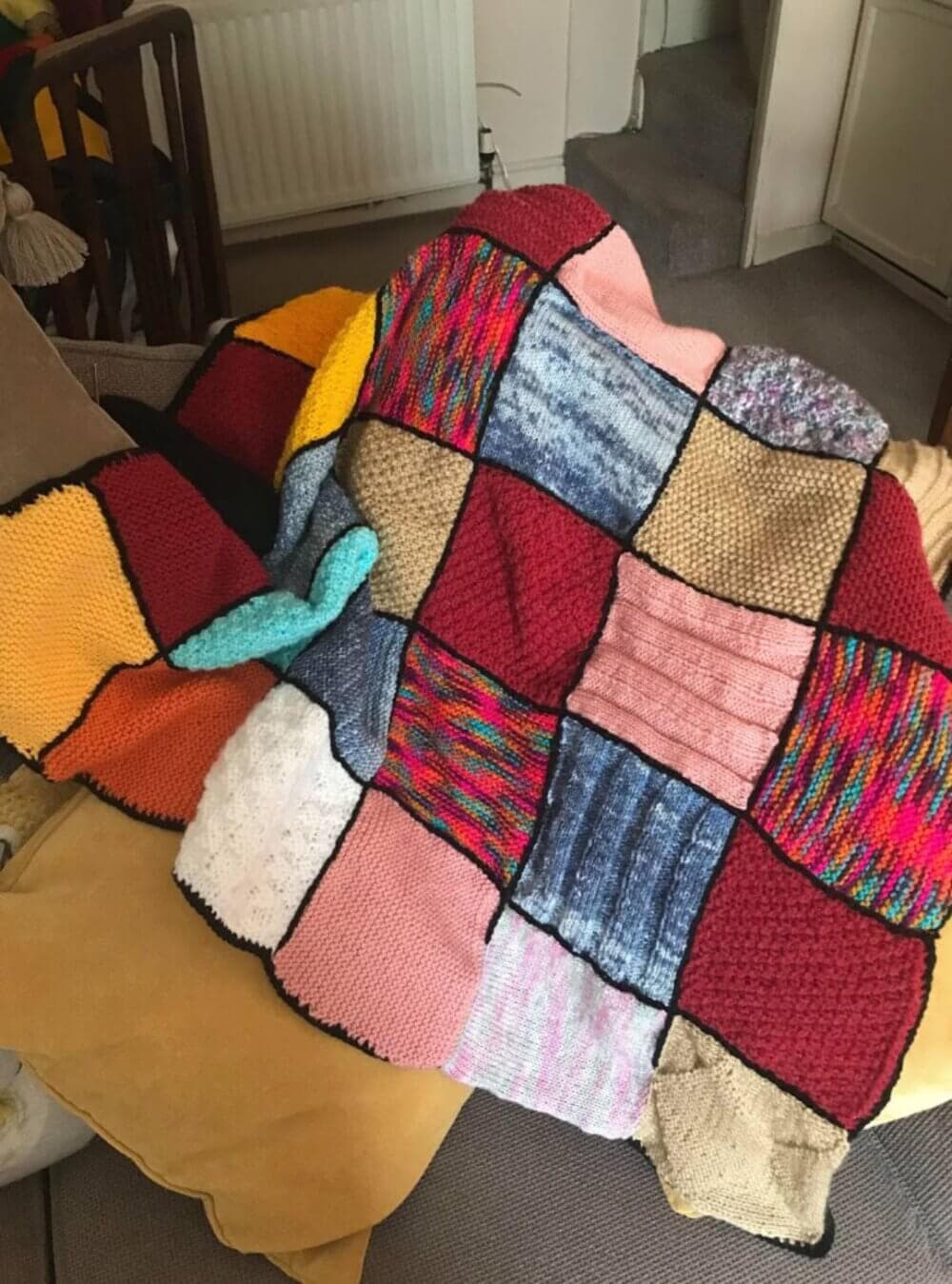 A colorful patchwork blanket made of various knitted squares is draped over a beige couch. - Home Instead