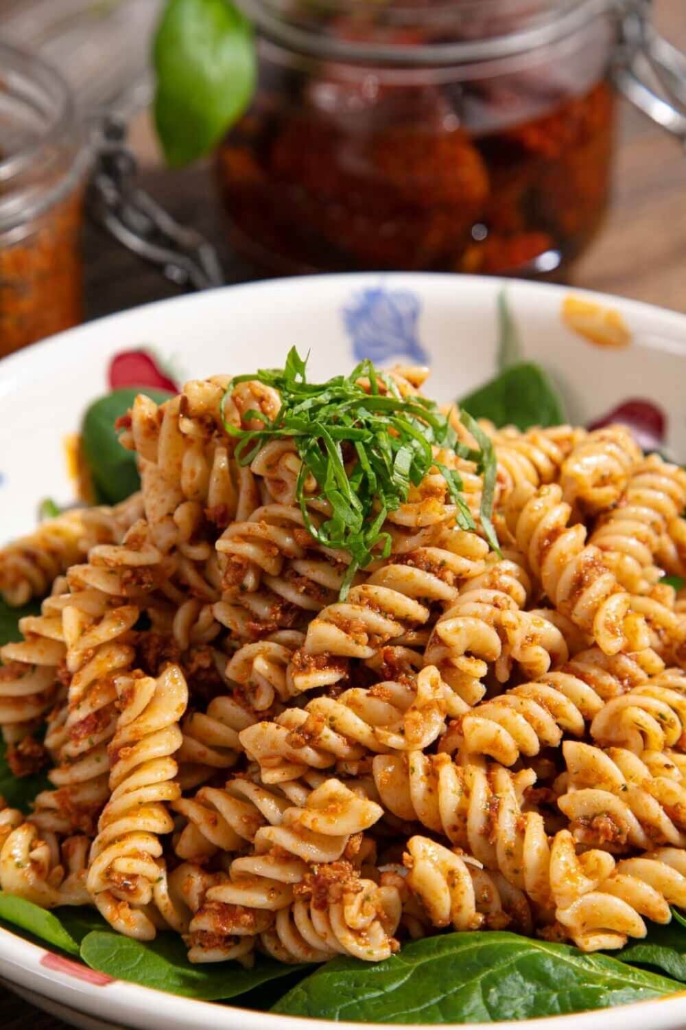 A bowl of seasoned spiral pasta garnished with fresh herbs and placed on a bed of greens. - Home Instead