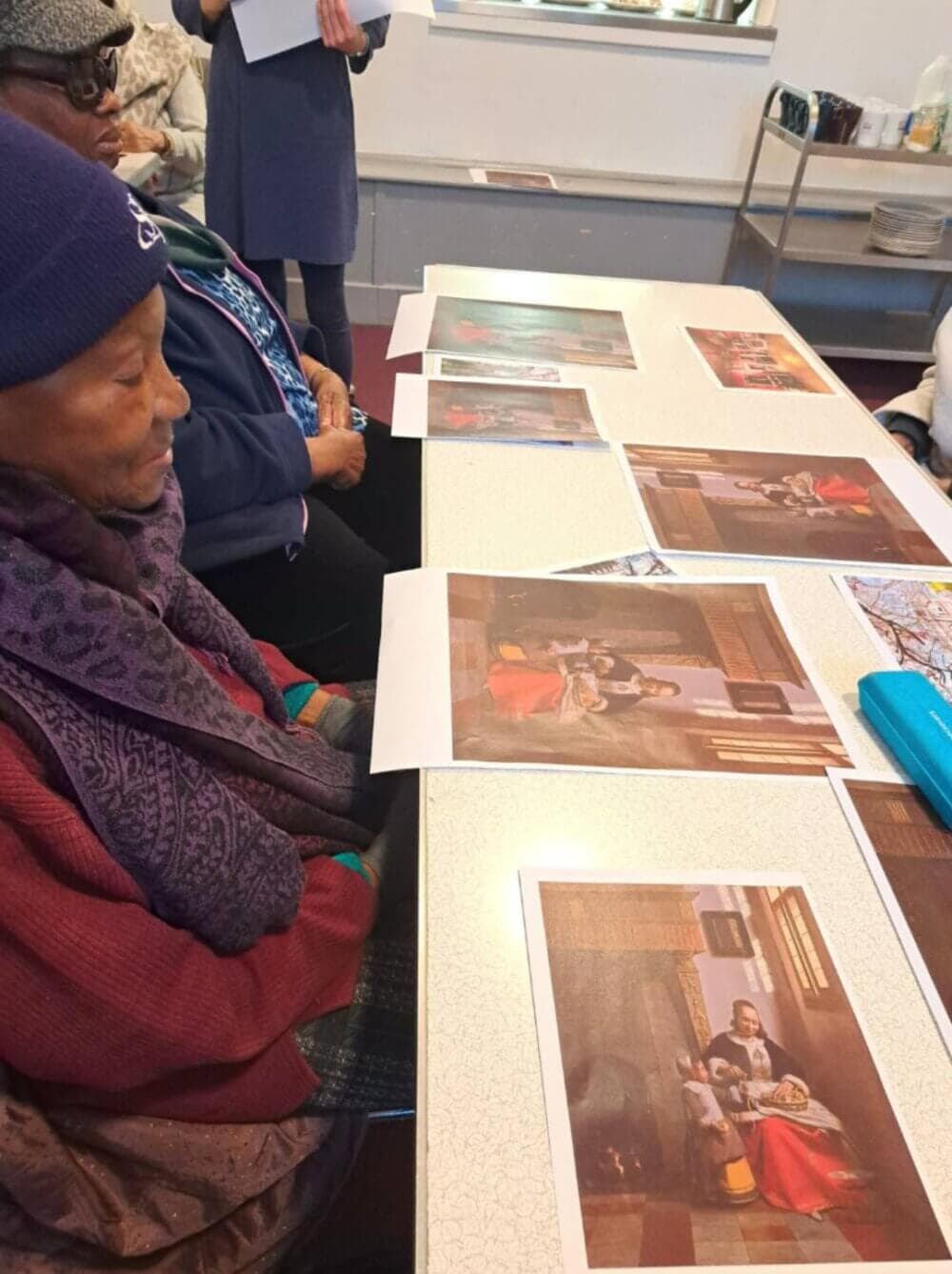 A group of people sits at a table looking at various art prints laid out in front of them. - Home Instead