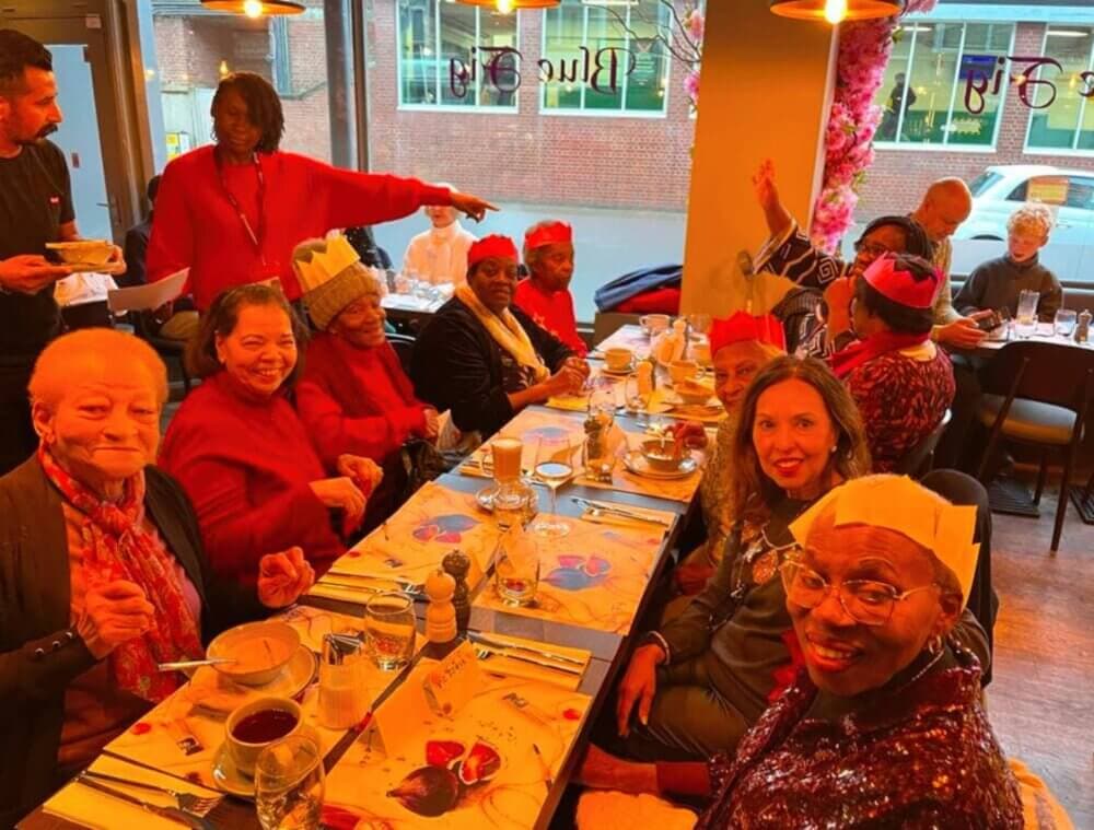 Group of people wearing festive hats sitting around a restaurant table, smiling and enjoying a meal together. - Home Instead