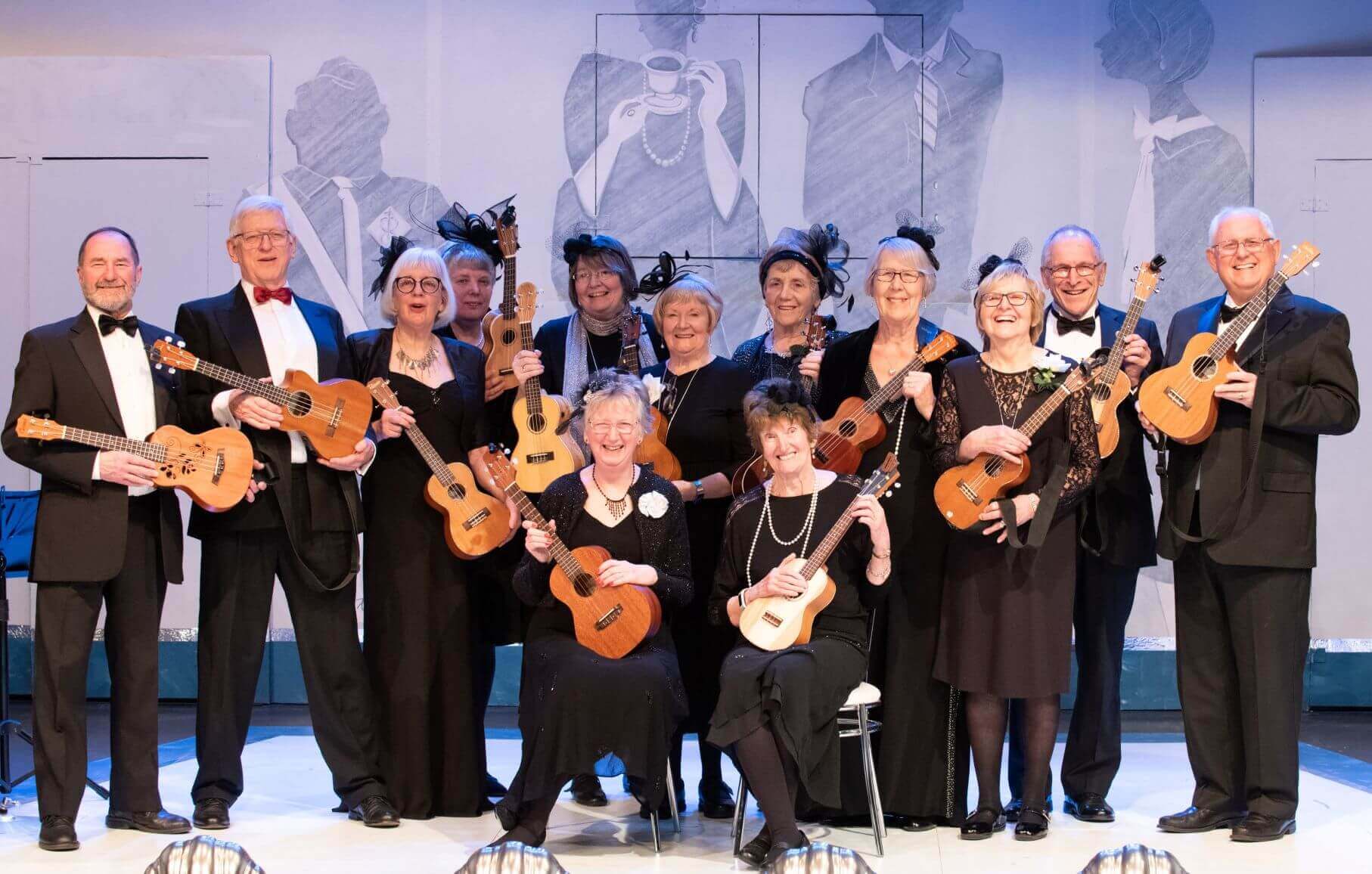 A group of older adults dressed formally, posing with ukuleles against a backdrop with painted figures. - Home Instead
