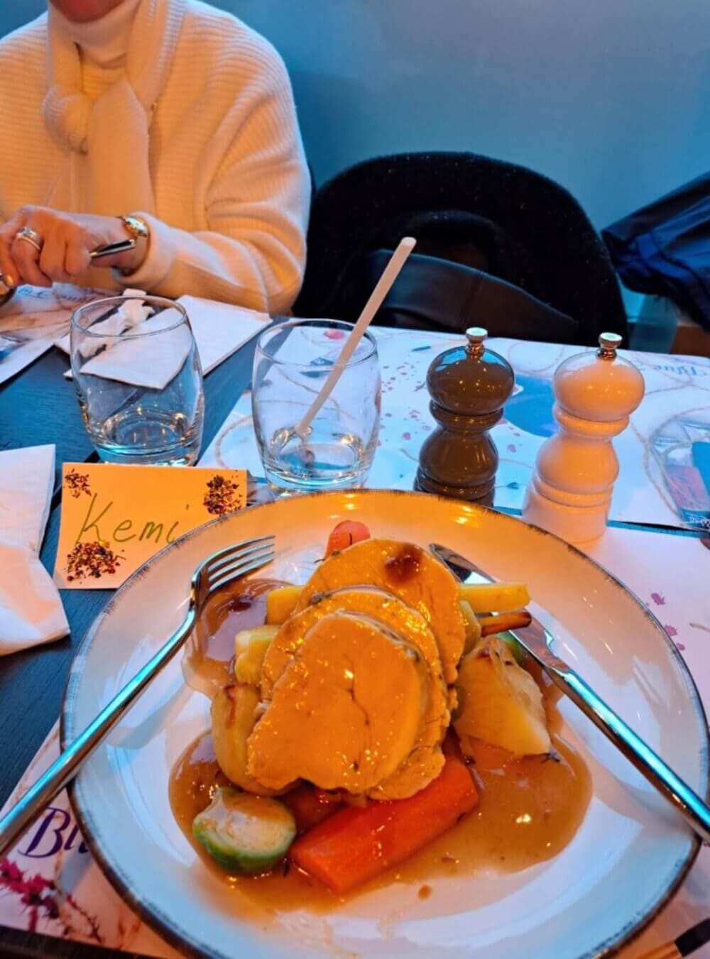 A person in a white sweater sits at a table with grilled vegetables and meat on a plate. Seasoning shakers are in the background. - Home Instead