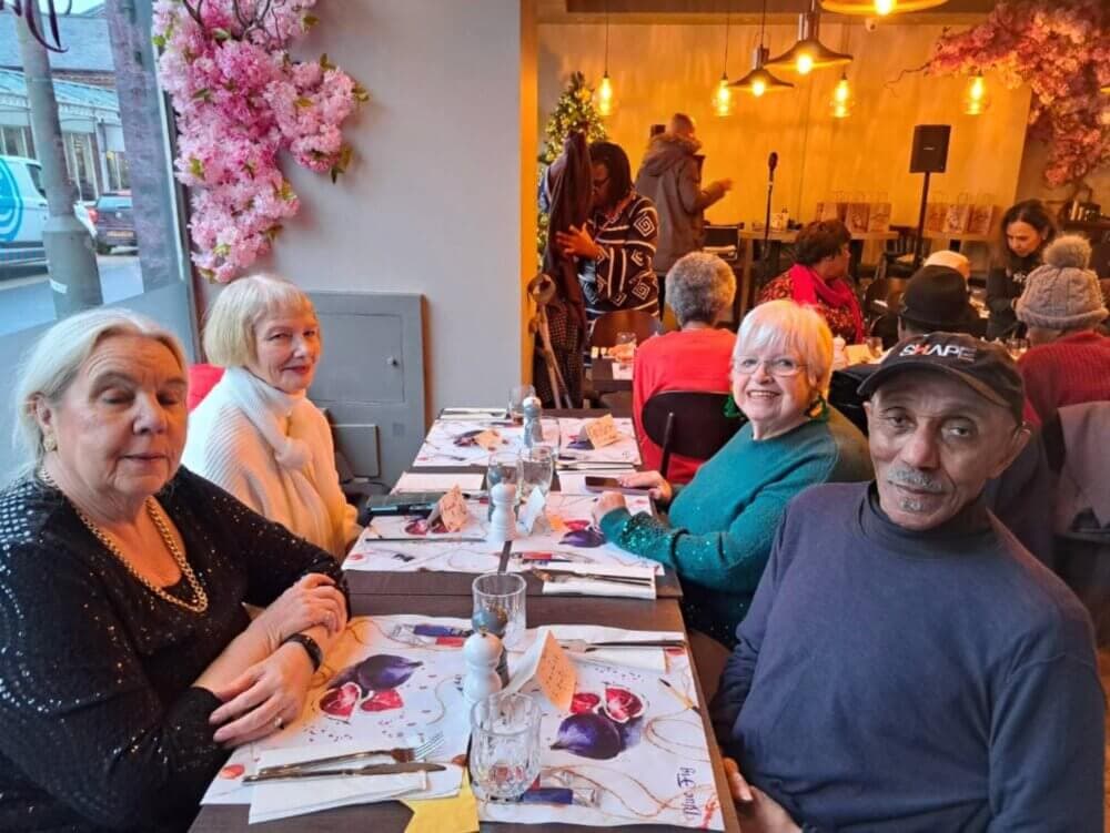 Four elderly people sitting around a table in a cozy restaurant with floral decorations. - Home Instead