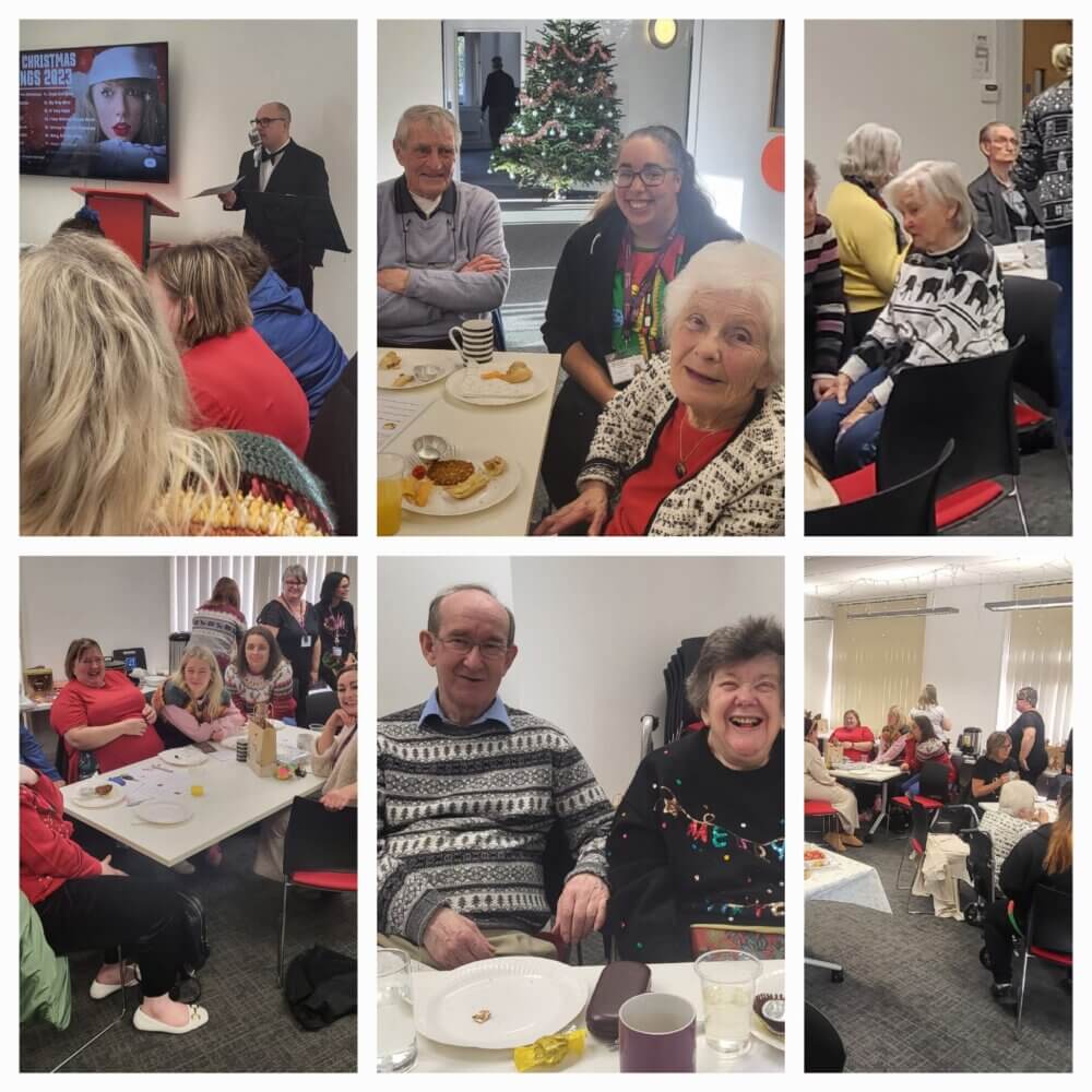 People of various ages attending a festive gathering, eating and socializing, with a presentation and holiday decorations in view. - Home Instead