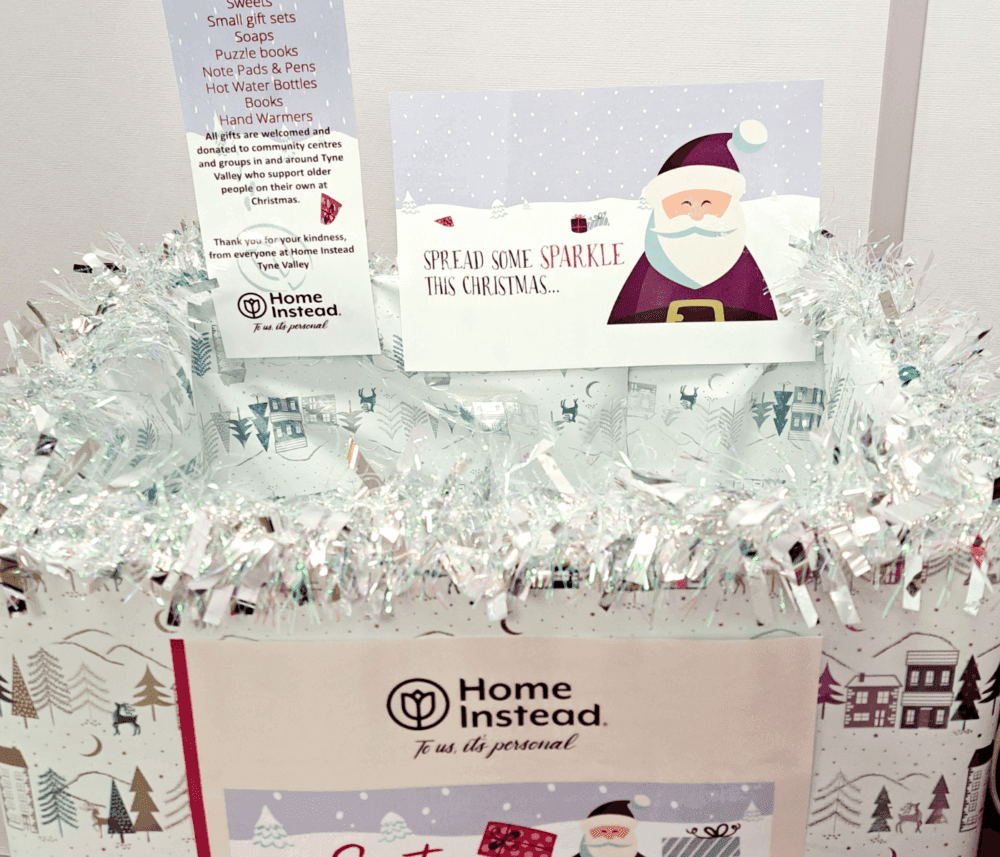 A festive donation box with a card that reads "SPREAD SOME SPARKLE THIS CHRISTMAS" and a Home Instead logo. - Home Instead