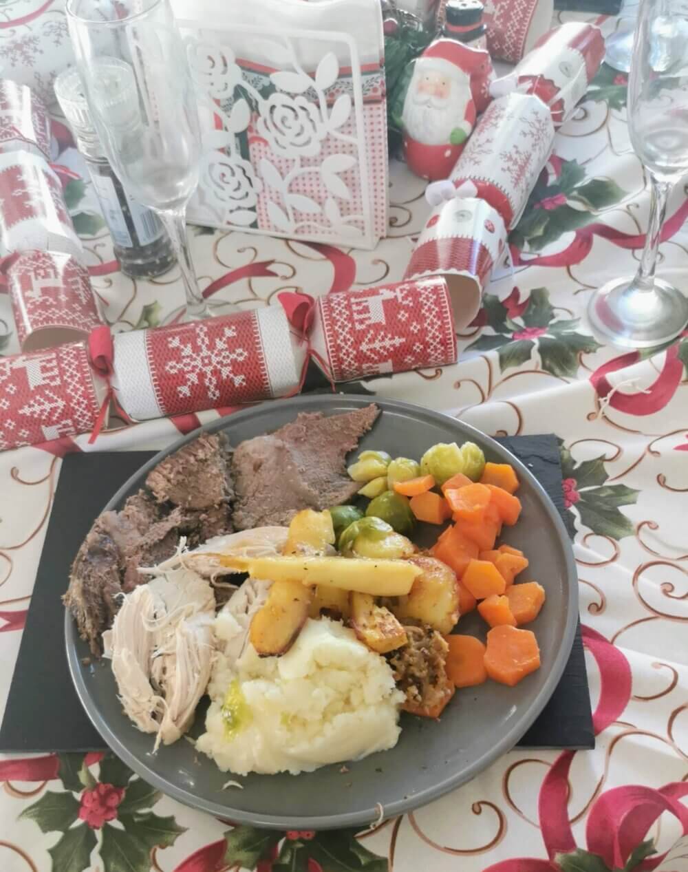 A Christmas dinner plate with roast beef, mashed potato, roasted vegetables, and decorations on a festive tablecloth. - Home Instead