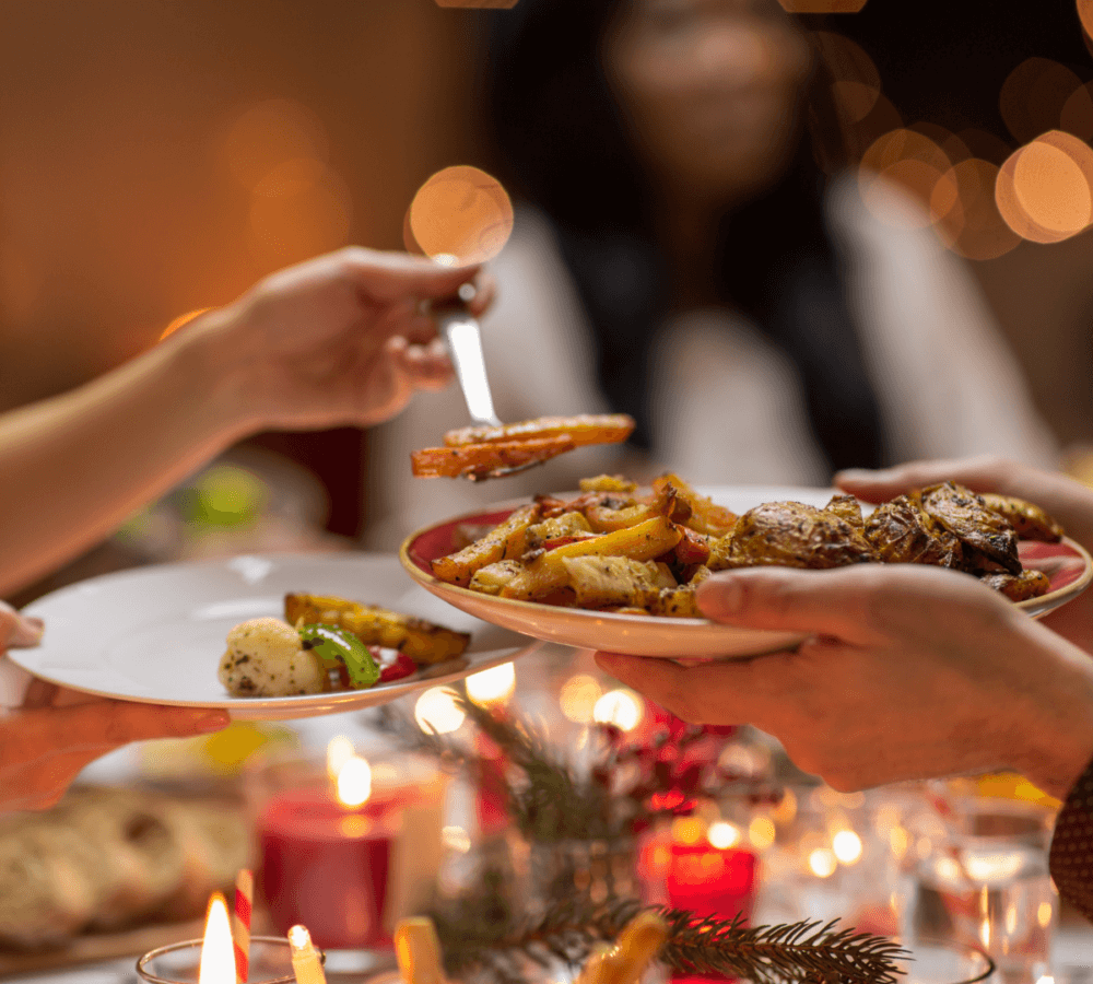 Close-up of a group sharing a festive meal, with one person serving food from a platter onto another's plate. - Home Instead