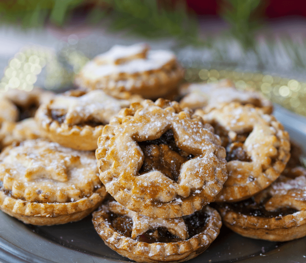 A plate full of powdered sugar-dusted mince pies, with star-shaped cutouts, arranged festively. - Home Instead