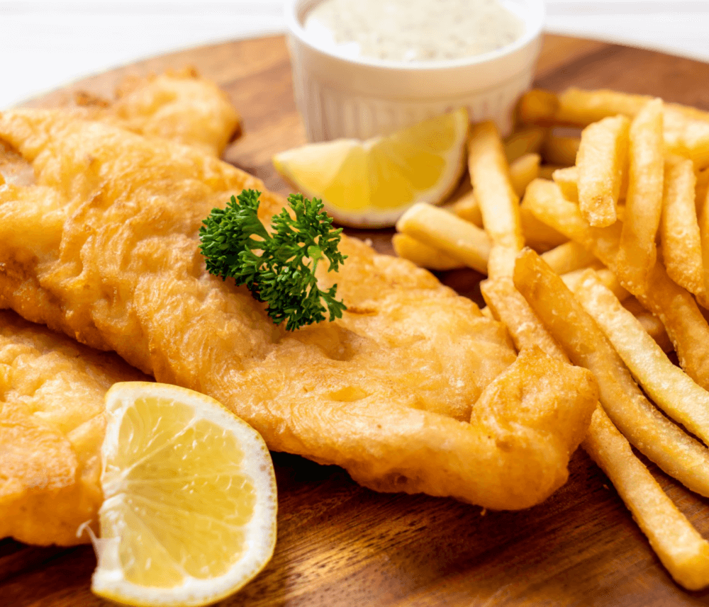 Battered fish fillet with french fries, garnished with parsley and lemon slices, served with a side of sauce. - Home Instead