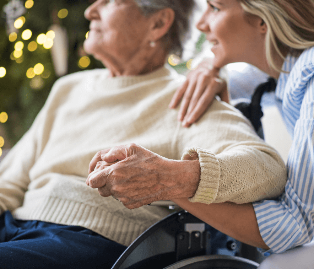 Older person in a wheelchair holding hands with a younger person; both look forward with warmth and togetherness. - Home Instead