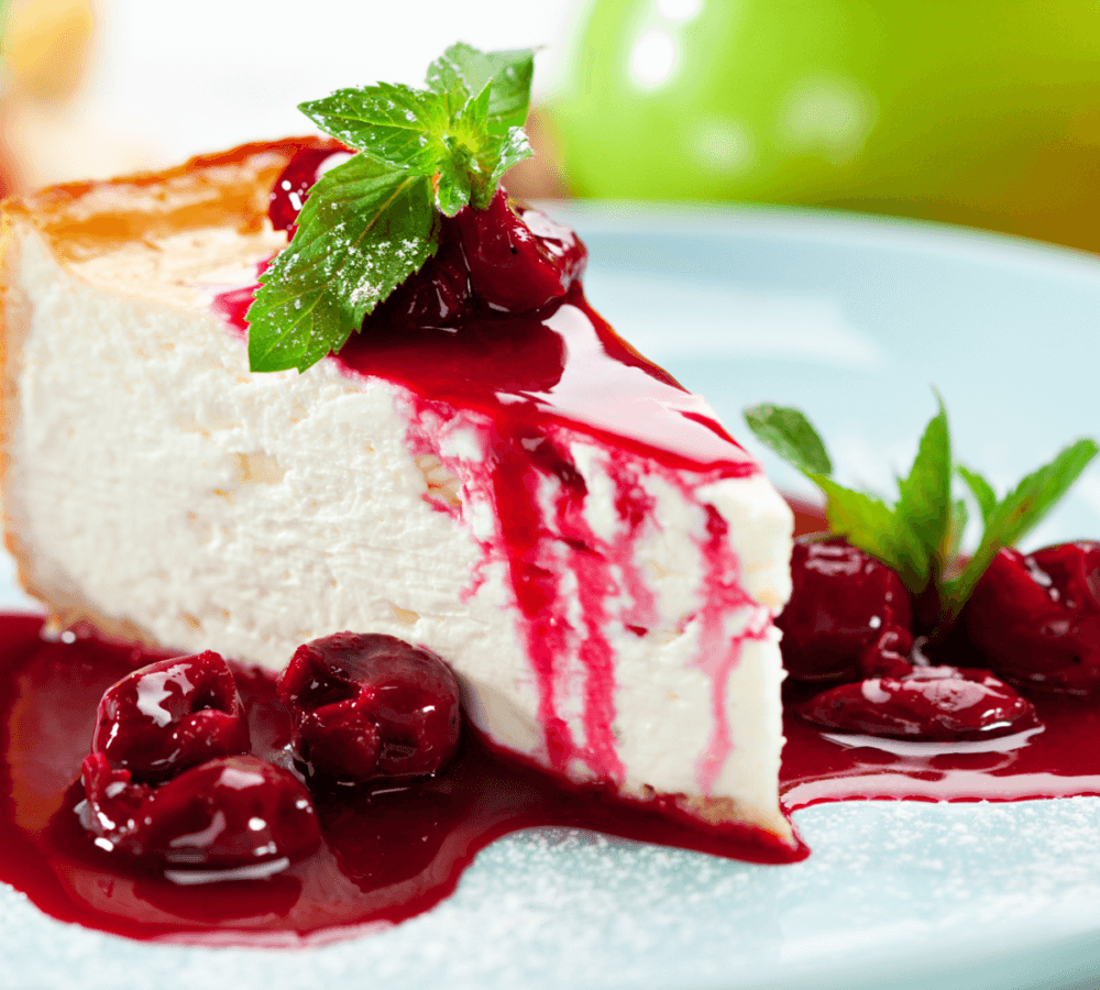 A slice of cheesecake with a cherry sauce drizzle, garnished with mint leaves, served on a light blue plate. - Home Instead