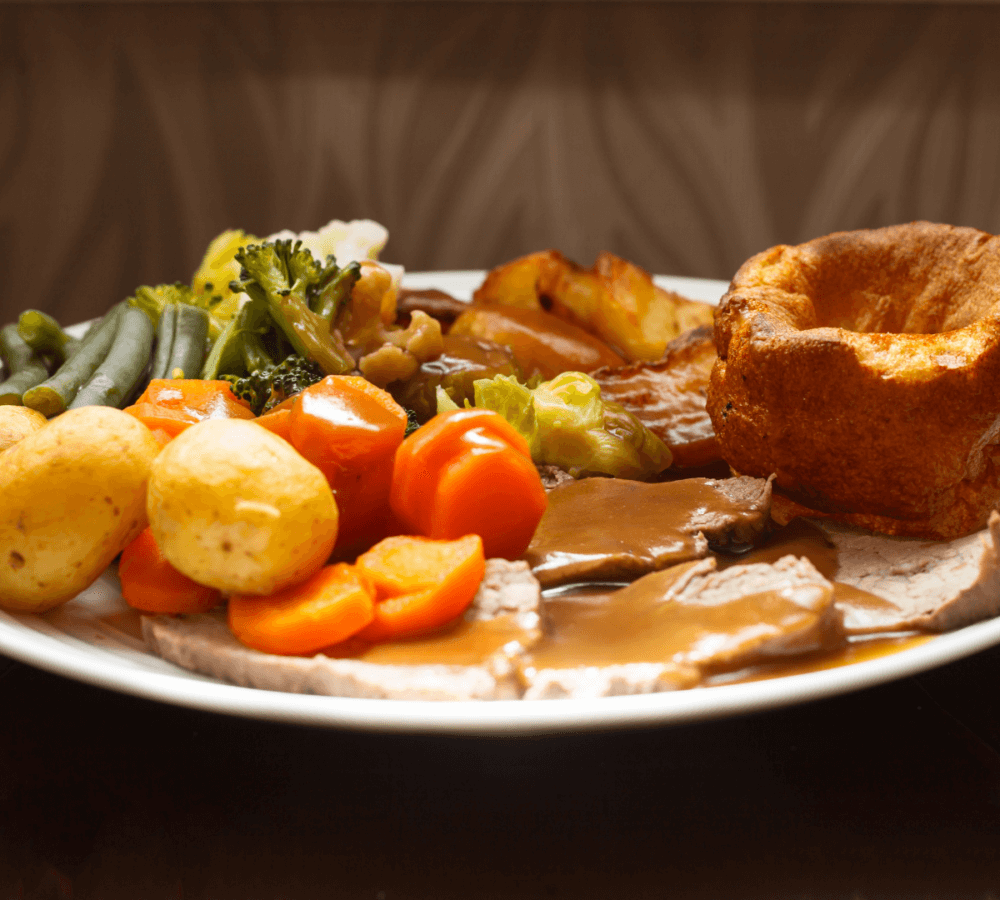 A plate of roast beef, potatoes, carrots, green beans, broccoli, and Yorkshire pudding with gravy. - Home Instead