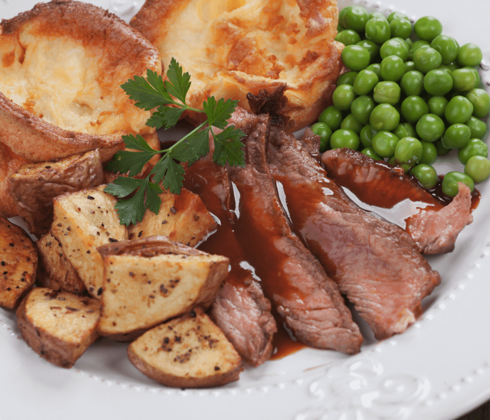 A plate of roast beef with gravy, roasted potatoes, peas, and Yorkshire pudding garnished with parsley. - Home Instead