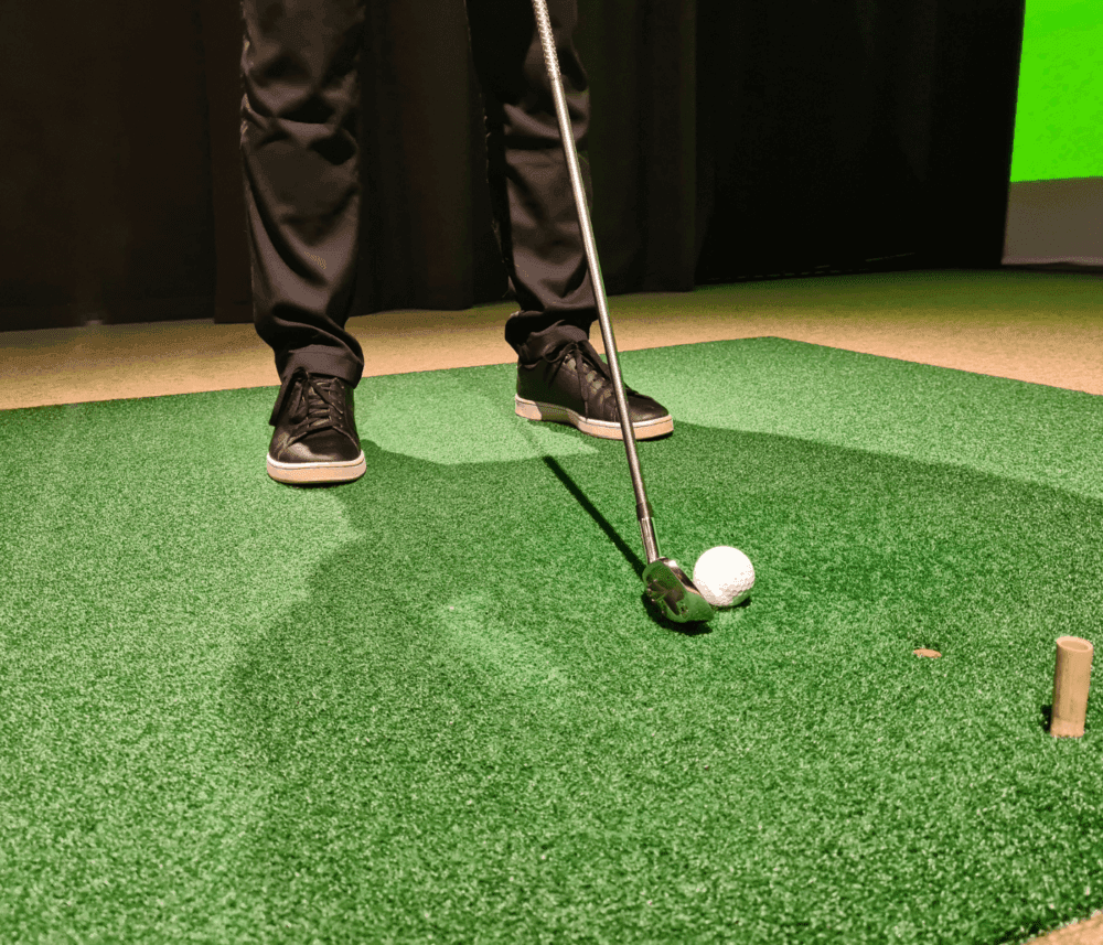 Person putting a golf ball on artificial turf with a putter, only lower legs and feet visible. - Home Instead